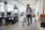 A man walking in an open office floor with his bike, smiling.