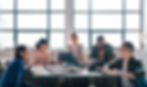A diverse team sitting together in a modern office lounge, collaborating on laptops and enjoying a lively discussion.