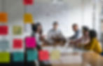 Group of colleagues having a meeting in a conference room with sticky notes on the glass wall.