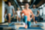 A diverse group of people smiling while doing step aerobics in a gym.