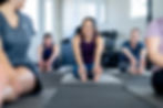 A group of people in a yoga class stretching on mats, smiling and enjoying the session in a bright studio.