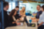 A group of professionals laughing and collaborating around laptops in a bright office setting