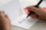 Hands writing thank you on a greeting card, placed on a table with an envelope nearby