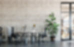 Industrial-style office with modern furniture, large plants, and design blueprints, creating a sleek and minimalist workspace.