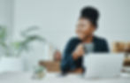 Smiling young woman holding a mug of coffee, sitting at her laptop in a modern office.