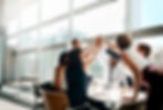 Group of colleagues enthusiastically high-fiving around a conference table in a bright office