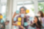 Two coworkers posting post-its on a see-through wall during an ideation session