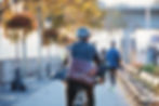 A professional wearing a helmet and suit rides a bicycle with a leather bag in an urban setting.