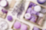 Lavender-themed gift box containing bath bombs, soap, and aromatic candles on a wooden surface.