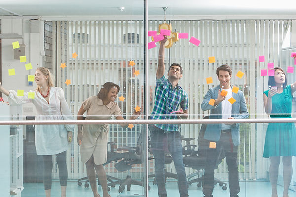 Five colleaguA team of professionals collaborating in a brainstorming session with sticky notes on a glass wall.